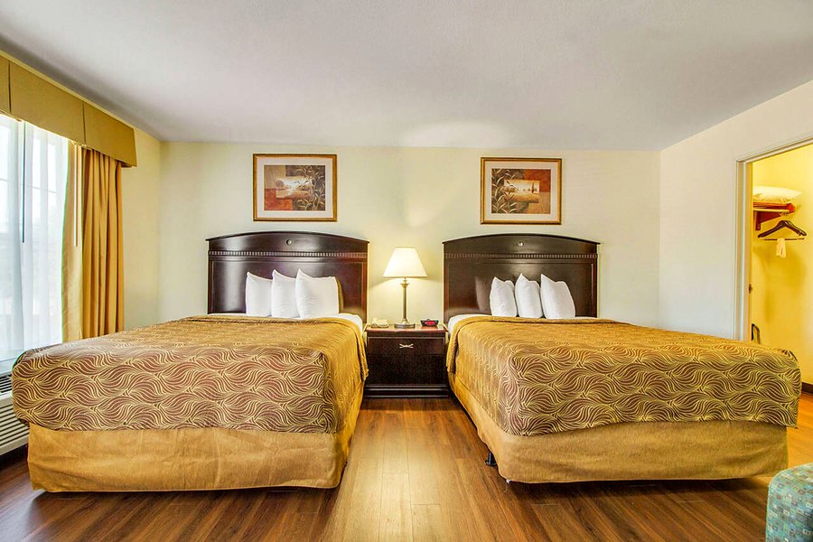 Suite with two queen beds side by side, a lamp between them and a curtained window.